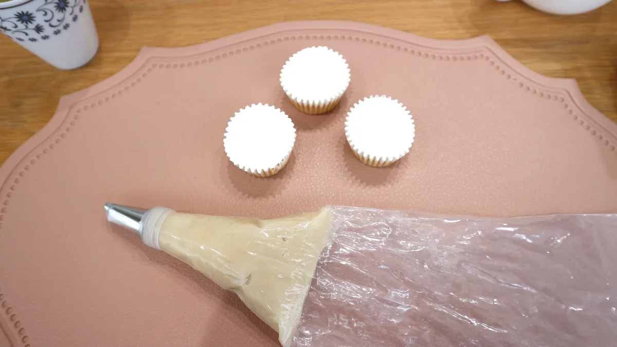 絞り袋にはいった白あんをきなこのカップケーキの上に絞っていく