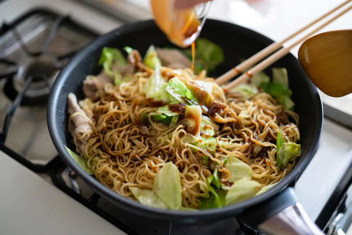 フライパンで焼きそばを炒め、ソースを加えて味をつける